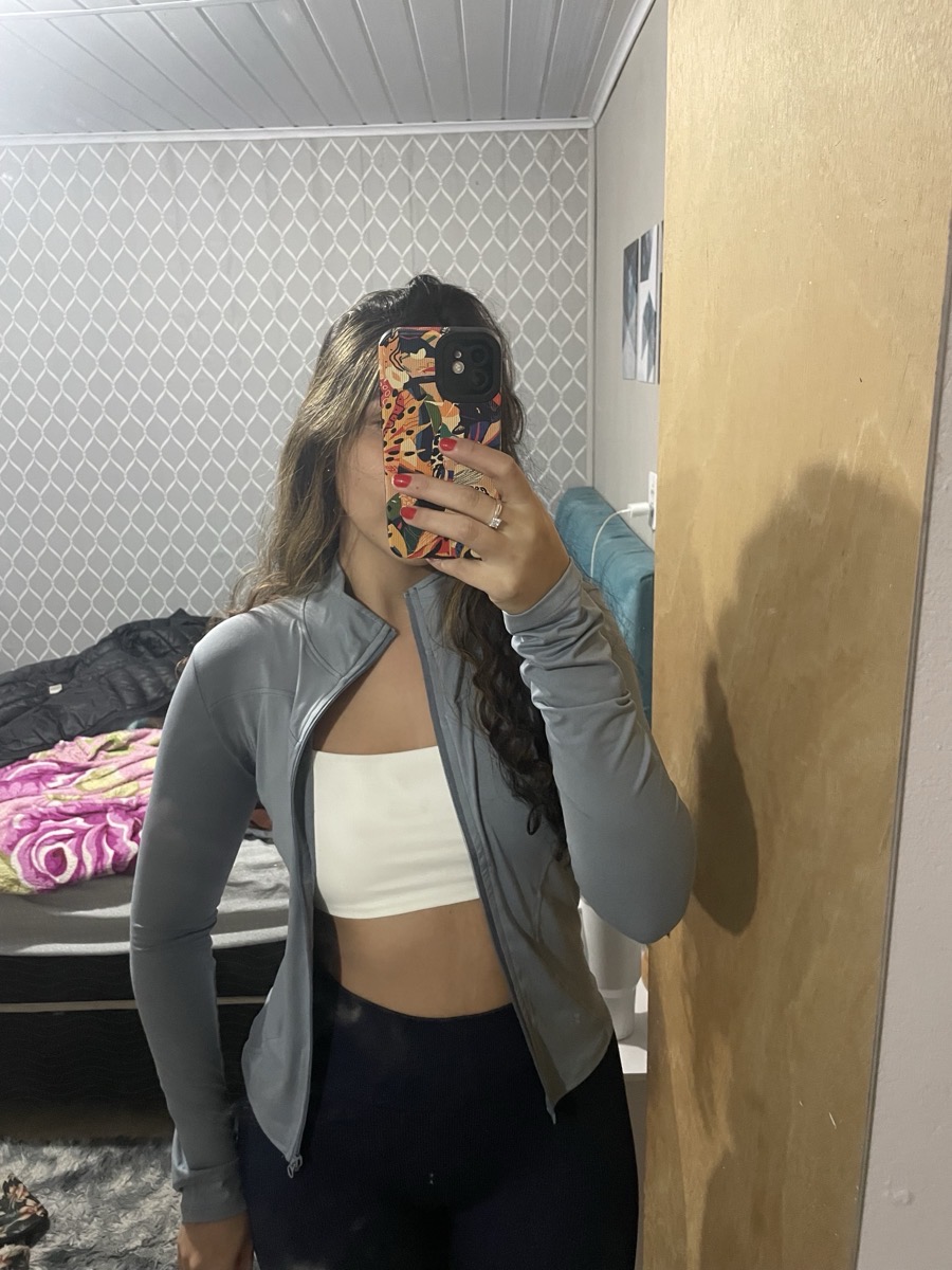 Foto no espelho de mulher vestindo jaqueta esportiva cinza aberta sobre top branco