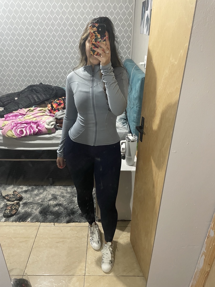 Foto no espelho de mulher vestindo jaqueta esportiva cinza e calça legging