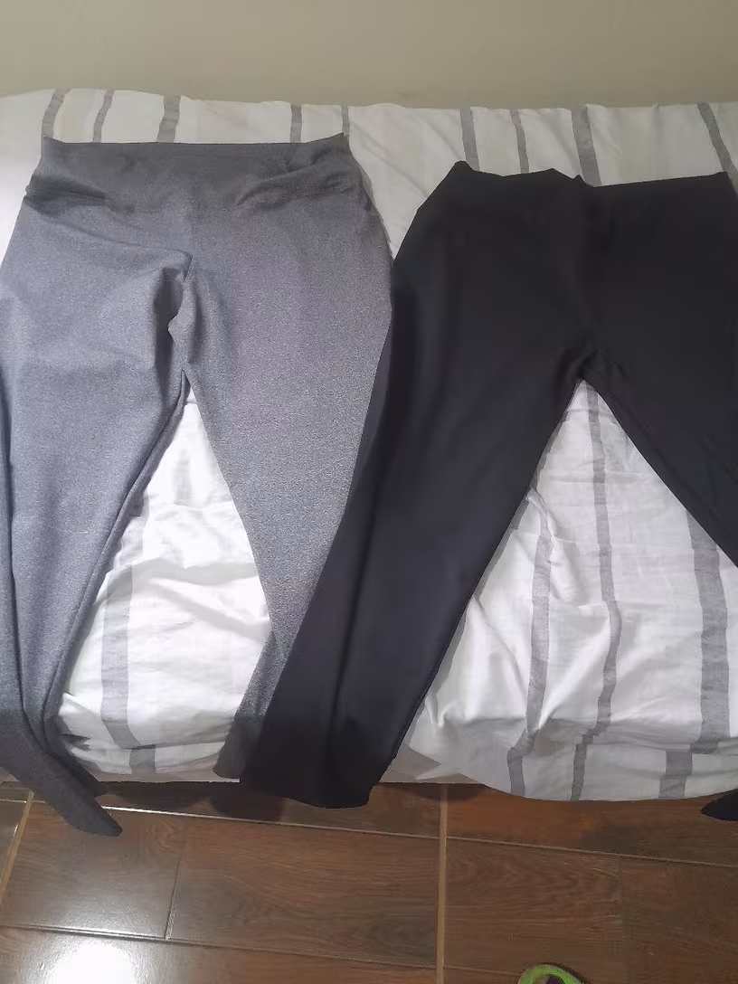 Duas calças legging, uma cinza e uma preta, estendidas lado a lado sobre uma superfície clara.
