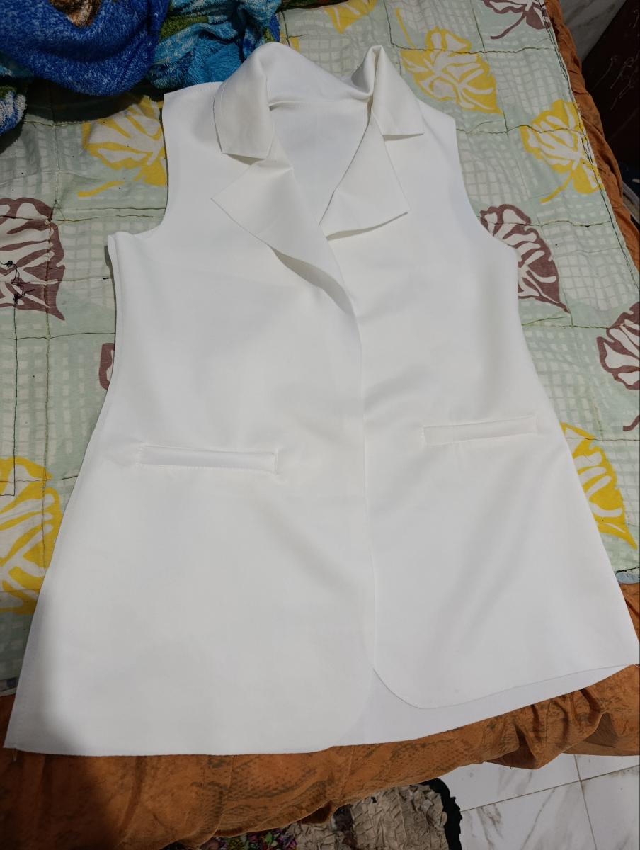 Colete feminino longo na cor branca estendido sobre uma colcha estampada