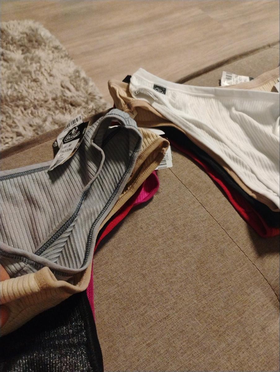 Mão segurando e exibindo o interior e acabamento interno de calcinhas tanga de cores variadas