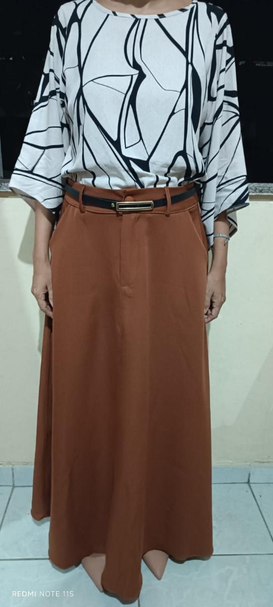 Mulher vestindo uma saia longa cor terracota com cinto preto e blusa estampada em preto e branco